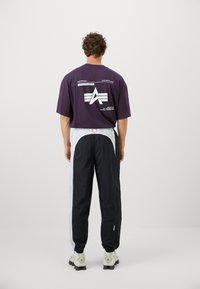 Lilla grafisk t-shirt med print på ryggen, parret med sorte og grå tapered bukser med elastisk talje og logo-detalje. Hvide sneakers.