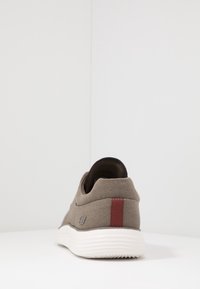 Šedé plátěné slip-on tenisky s bílou podešví, texturovaným svrškem a vínovým akcentem na patě. Na boku se nachází logo.