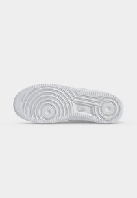 Λευκή σόλα αθλητικού παπουτσιού Nike με κυκλικά σχέδια πέλματος και λογότυπο Nike στο κέντρο σε απλό φόντο.