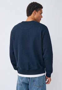 Mörkblå sweatshirt i bomullsblandning med ribbade muddar och fåll, med en avslappnad passform och en slät yta. Inga synliga tryck.