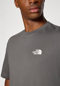 Gray cotton t-shirt featuring a crew neck and short sleeves, with a white logo on the left chest area. Smooth texture, regular fit.