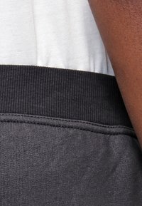 Dunkelgraue Sweatpants mit einem gerippten schwarzen Bund. Der Stoff wirkt weich und glatt und zeigt schlichte Nähte entlang des Bundes.