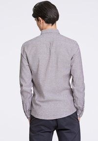 Camisa larga de mangas con textura gris, cuello abotonado y dobladillo curvo. Presenta puños con botones y un patrón sutil para un detalle adicional.