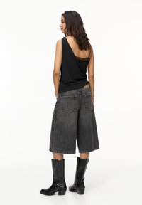 Black draped tank top over lace camisole, paired with gray wide-leg denim shorts and knee-high black leather boots.