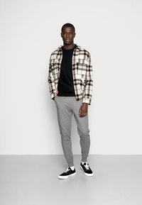 Geruite shirt in wit, zwart en geel, zwarte sweatshirt, slimfit grijze joggingsbroek en zwarte sneakers met witte zolen. Eenvoudige maar functionele outfit.