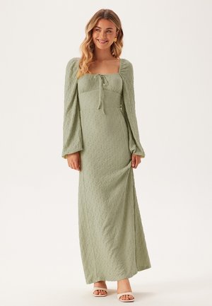 Maxi-jurk van lichtgroene textuurstof, met een vierkante halslijn, opgezette lange mouwen en een strik aan de voorkant. Elegante en getailleerde stijl.