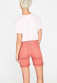 Pantalones cortos de mezclilla rosa con dobladillos enrollados, que cuentan con bolsillos traseros y detalles de costura sutiles. Combinados con una camiseta de color rosa claro.