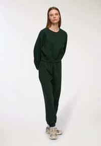 Ciemnozielony sweatshirt i dopasowane dresy, wykonane z miękkiego materiału, o luźnym kroju, z elastycznymi mankietami i paskiem w talii. Sneakersy o wzorzystym designie.