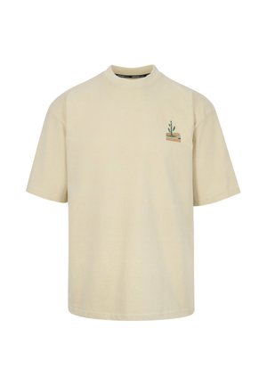 Beiges T-Shirt mit kurzen Ärmeln, das auf der linken Brustpartie ein kleines grünes Kaktus- und braunes Wüstendesign zeigt.