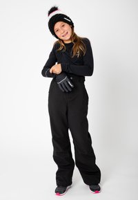 Zwarte sneeuwbroek met verstelbare banden, gecombineerd met een zwarte longsleeve en zwarte handschoenen. De zwarte gebreide beanie heeft een roze en witte pompon.