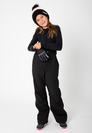 Pantalons de neige noirs avec des bretelles réglables, associés à un haut noir à manches longues et des gants noirs. Le bonnet en tricot noir est orné d'un pompon rose et blanc.