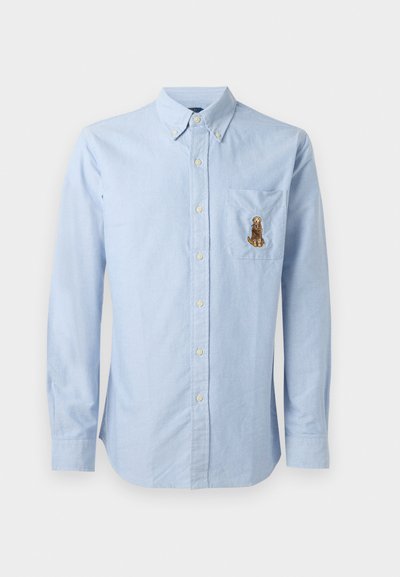 Gai zila pogu krekls ar garām piedurknēm, krūšu kabata ar brūnu izšuvumu dzīvnieka motīvā, izgatavots no mīksta auduma.