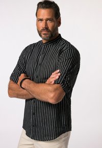 Camisa de manga corta a rayas blancas y negras con cuello de camisa, que presenta un cierre de botones y un corte relajado. Se lleva con pantalones de color claro.