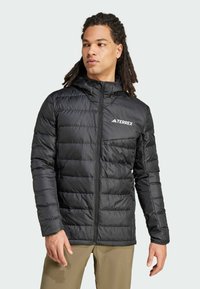 Veste noire matelassée avec fermeture éclair à l'avant, capuche réglable et logo TERREX sur la poitrine. Fabriquée en matériau lisse et résistant à l'eau.