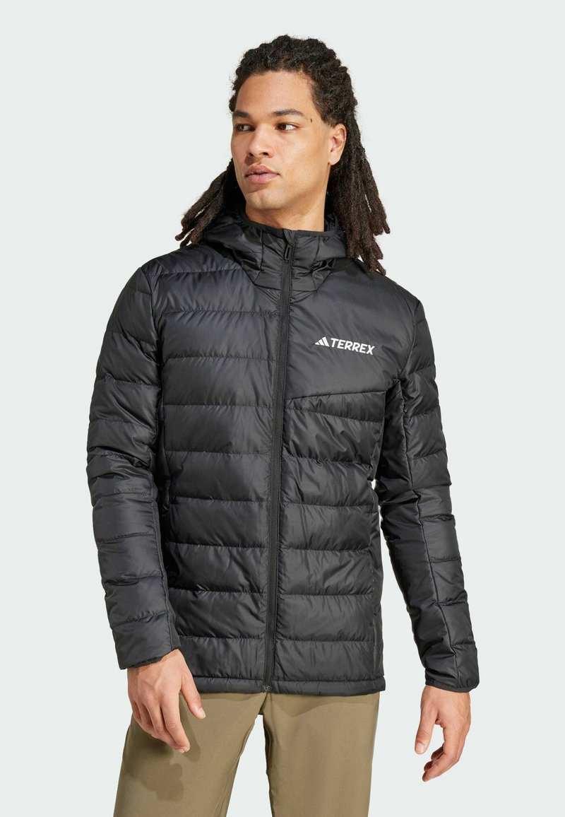 Veste noire matelassée avec fermeture éclair à l'avant, capuche réglable et logo TERREX sur la poitrine. Fabriquée en matériau lisse et résistant à l'eau.