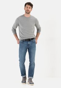 Chemise à manches longues grise, jeans en denim bleu, ceinture noire, baskets grises. Coupe décontractée, denim confortable, poignets côtelés sur la chemise, design simple.