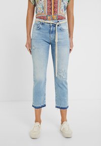 Jeans cortos de color azul claro con dobladillo deshilachado, detalles desgastados y acentos florales bordados. Combinados con un cinturón texturizado beige.