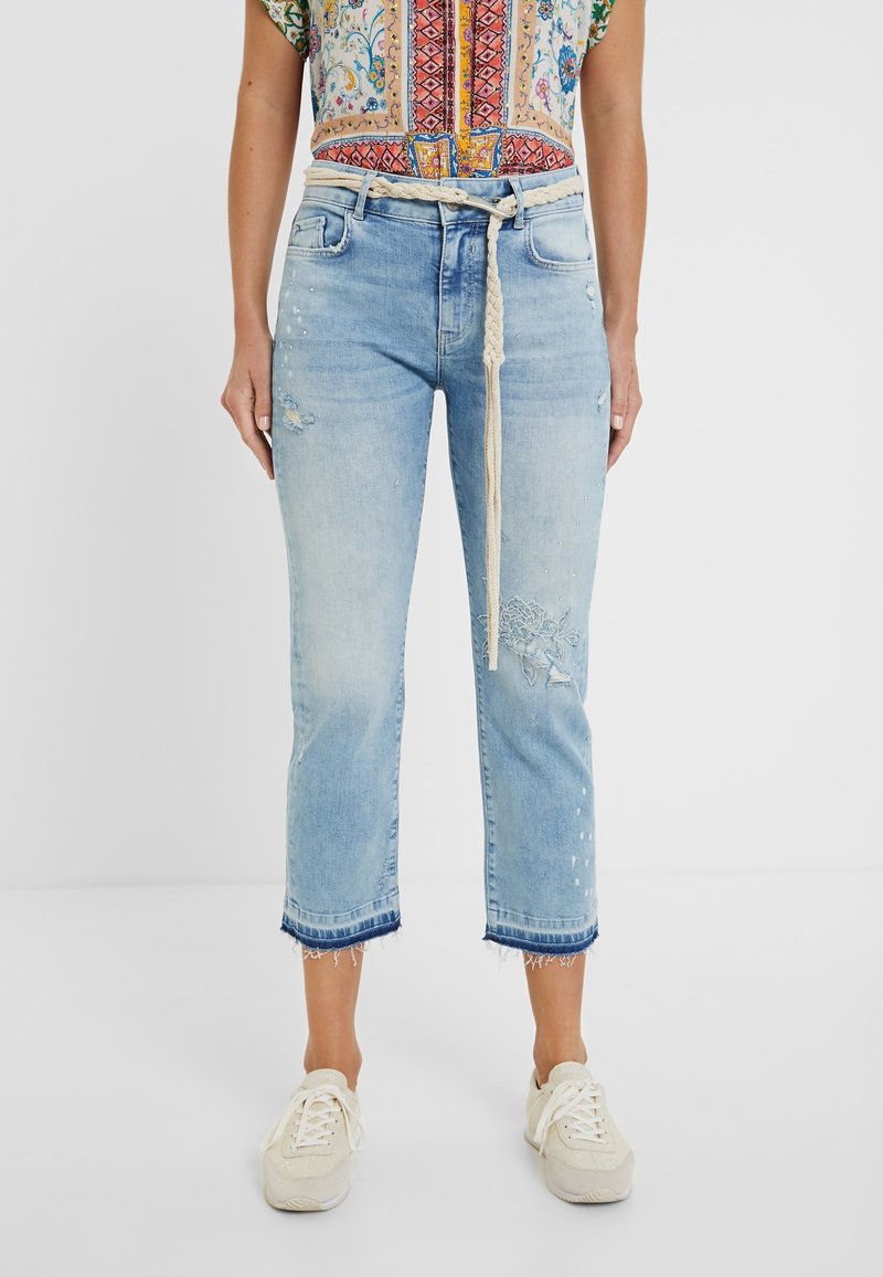 Jeans cortos de color azul claro con dobladillo deshilachado, detalles desgastados y acentos florales bordados. Combinados con un cinturón texturizado beige.