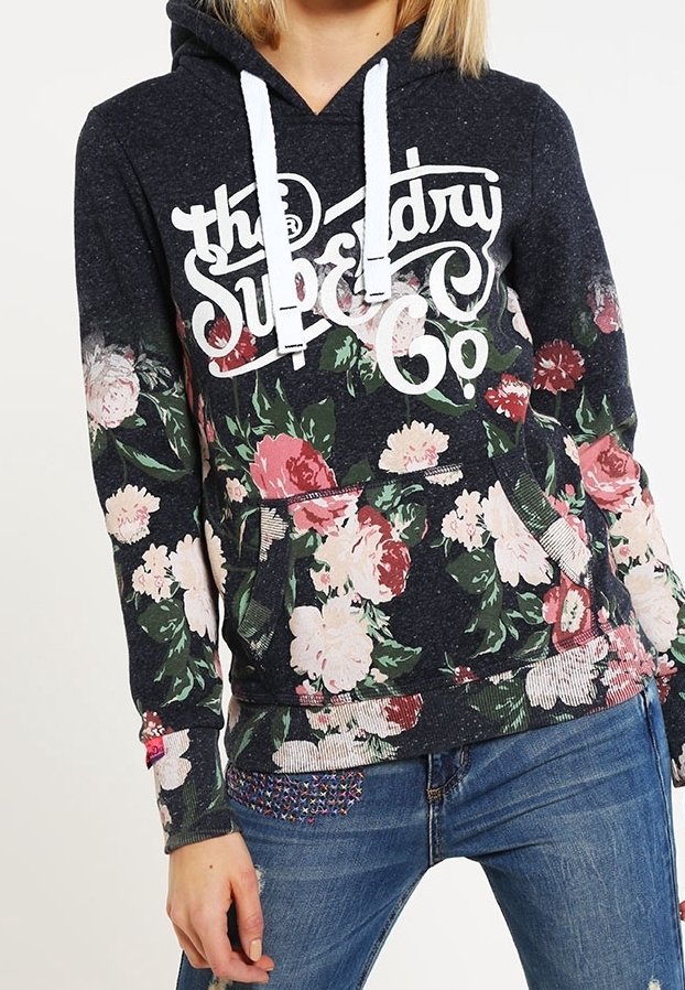 Sudadera con patrón floral sobre una base azul oscura, con cordones blancos y puños acanalados. Cuenta con un bolsillo frontal y un logo en blanco.