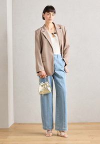 Beige oversized blazer, witte geribbelde top, lichtblauwe wijde jeans, zilverkleurige metallic mini tas en gespenhakken. Gladde texturen, modern ontwerp.
