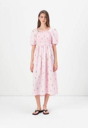 Vestito rosa di lunghezza midi con maniche a sbuffo e scollo quadrato. Presenta un corpetto arricciato e motivi floreali su tutta la superficie. Indossato con ciabattine nere.