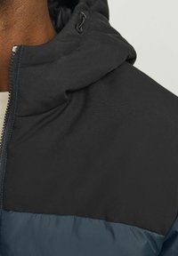Black and dark blue puffer jacket with a zippered front, adjustable hood, and smooth texture; features contrast stitching and a snug fit.