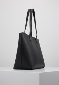 Sac fourre-tout en cuir noir avec une forme structurée, deux anses épaules et une fermeture éclair. Texture lisse avec des accents métalliques minimalistes.