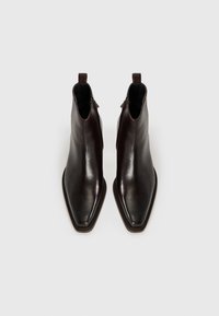 Botas de tobillo de cuero marrón oscuro con una puntera afilada, textura suave y cremalleras laterales; cuentan con un pequeño lazo en el talón para ponérselas fácilmente.