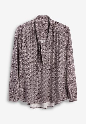 Blouse à manches longues avec imprimé léopard mauve et blanc, col froncé et tissu doux tombant sur un fond blanc.
