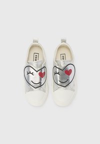 Des chaussures argentées à enfiler avec de grands motifs en forme de cœur arborant des visages souriants, des cœurs rouges, des semelles en caoutchouc blanches et une finition texturée.