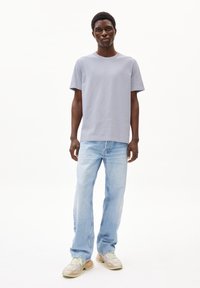 Hellgraues Baumwoll-T-Shirt, klassischer Schnitt, kombiniert mit hellblauen geraden Jeans und gemusterten Sneakers. Einfaches Design, weiche Textur.