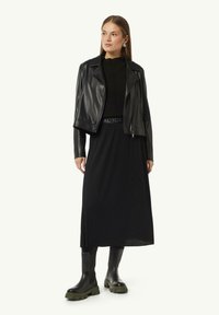 Black leather cropped jacket over a black ribbed top and long skirt, paired with black chunky boots featuring green soles.