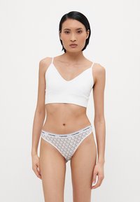 Hvit bomulls bralette med V-hals og tynne stropper, kombinert med lysegrå mønstrede truse med merkevare midjebånd.