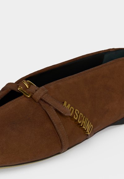 Καφέ καστόρινo μυτερό μοκασίνι με χρυσή αγκράφα και λογότυπο MOSCHINO από χρυσά γράμματα στο πλάι, με χαμηλή μαύρη σόλα.