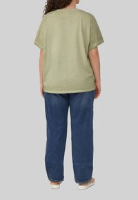 Olivengrünes oversized T-Shirt mit kurzen Ärmeln, weichem Material, rundem Ausschnitt und sichtbaren Nähdetails, kombiniert mit lockeren blauen Jeans.
