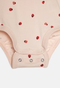 Einen cremefarbenen Bodysuit mit rotem Marienkäferdruck, der über einen Druckknopfverschluss im Schritt verfügt und aus einem weichen Stoff für optimalen Tragekomfort besteht.