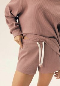 Różowa, prążkowana bluzka i szorty w zestawie, z elastycznym paskiem w talii i miękką strukturą. Wśród detali znajdują się białe akcenty sznurka.