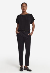 Sort, løstsiddende top med korte ærmer, parret med skræddersyede sorte bukser. Outfit inkluderer et slankt sort bælte og skinnende sorte sko.