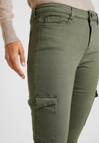 Pantalons cargo verts olive avec une coupe slim, dotés de poches latérales avec fermetures à bouton et d'une finition lisse et texturée.