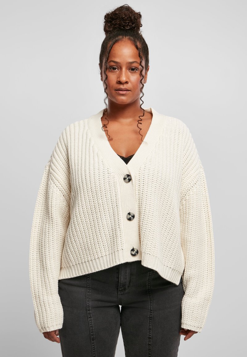 Krämfärgad stickad cardigan med V-hals, kort passform, stora svarta knappar och ribbade manschetter. Mönstrad textur och avslappnad silhuett.
