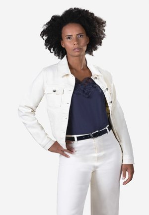 Giacca di denim bianco con due tasche frontali, top in pizzo blu navy e pantaloni bianchi a vita alta. Cintura nera con fibbia rotonda in argento. Tessuto testurizzato.
