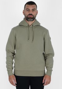 Felpa con cappuccio verde oliva in un tessuto morbido e testurizzato. Presenta stringhe di regolazione con punte metalliche e polsini e orlo a costine.