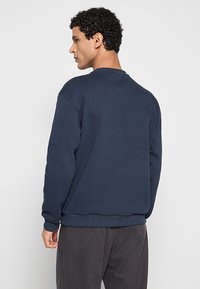 Marineblauwe sweatshirt met een ronde halslijn, geribde manchetten en een gestructureerde stof. Voorzien van een achterzak op de linkermouw.