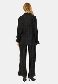 Conjunto de color negro con estampado que incluye una camisa de manga larga y pantalones de pierna ancha, fabricado con un tejido texturizado, con puños y un ajuste relajado.