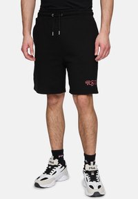 Pantaloni corti neri in cotone con vita elastica e coulisse; presenta un ricamo rosa "RSVP" sulla gamba sinistra. Abbinati a scarpe da ginnastica bianche.