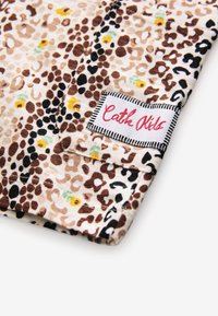 Leopardikuvioinen kangas, jossa on ruskean, mustan ja kerman sävyjä, sekä keltaisia ja vihreitä yksityiskohtia. Sisältää valkoisen merkin mustalla reunuksella.