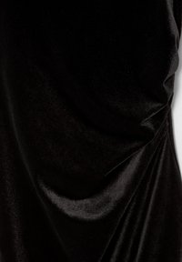 Tissu en velours noir avec une texture douce et lisse. Présente des détails drapés, créant une forme élégante avec un éclat subtil.