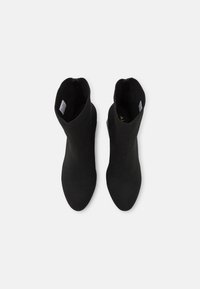 Botas negras de tobillo hechas de un tejido elástico, con un diseño de punta afilada y una superficie lisa con una silueta minimalista.