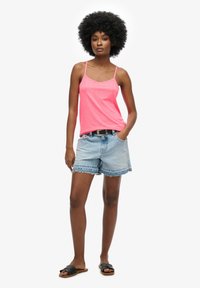 Top ligero de color rosa brillante con tirantes finos, combinado con unos pantalones cortos de denim azul claro con bordes deshilachados y sandalias negras tipo slide.