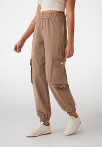 Bruine cargobroek met elastische tailleband, zijzakken en gathered cuffs. Gecombineerd met witte sneakers voor een casual uitstraling.